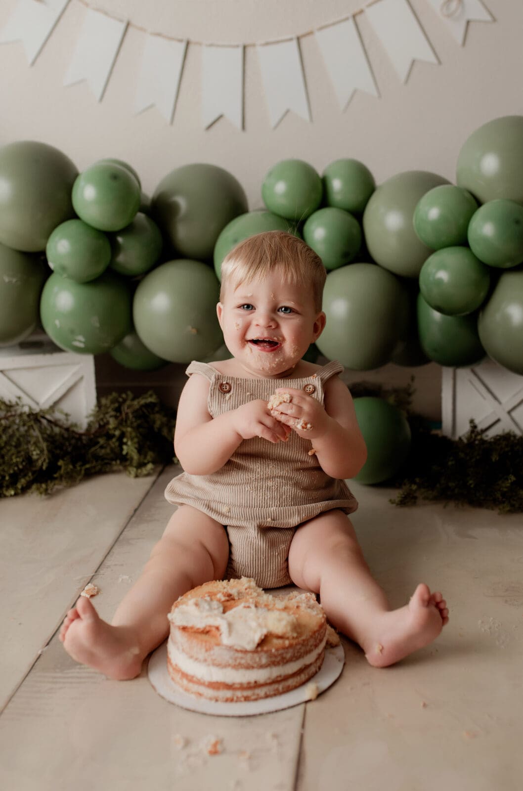 baby on first birthday with cake and green balloons