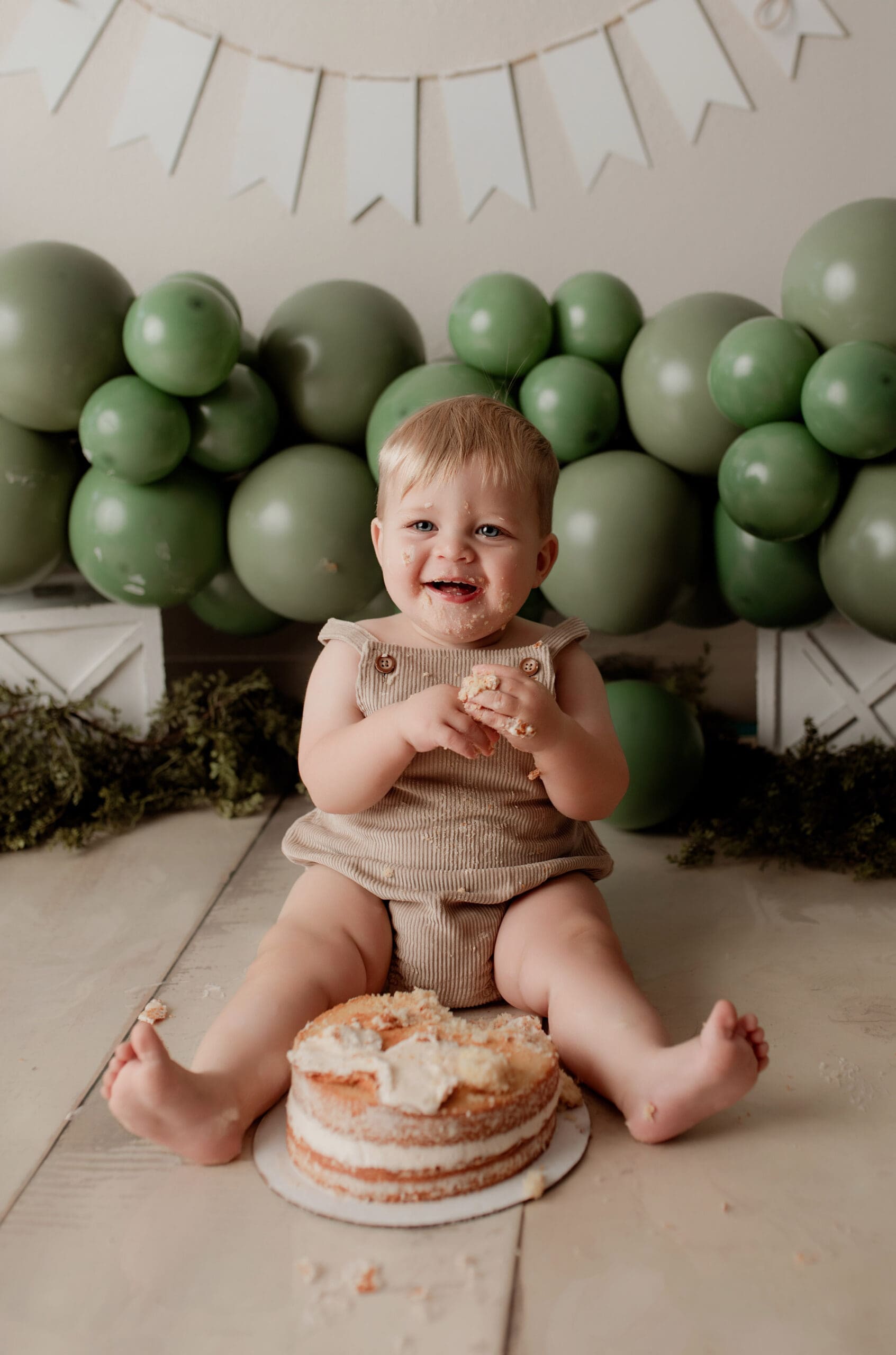 baby on first birthday with cake and green balloons